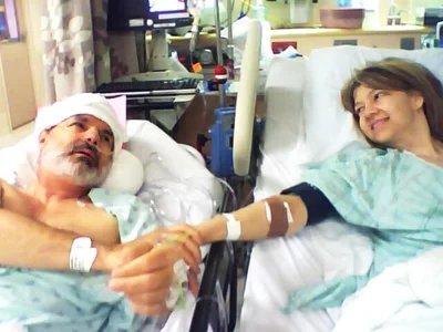 Jeff Moyer and Julie Stinson holding hands and smiling from adjacent hospital beds after his kidney donation, June 2010